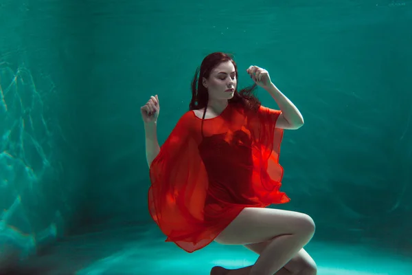 Amazing underwater portrait of a beautiful young woman in a orange dress. Girl swimming underwater — ストック写真