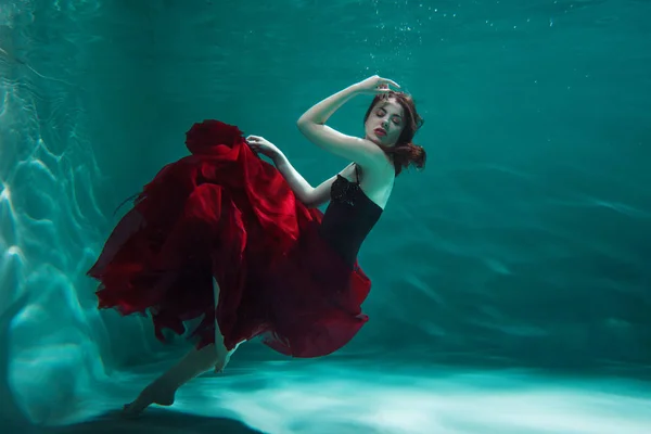 Schönes Mädchen in rotem Kleid schwimmt unter Wasser — Stockfoto