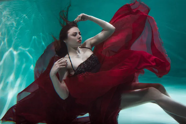 Mystisches Unterwasserporträt einer schönen jungen Frau in einem roten Kleid. Mädchen schwimmt unter Wasser — Stockfoto