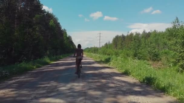 Chica en una bicicleta paseos en un camino de tierra en el pueblo. Ciclismo en la naturaleza, bosque . — Vídeo de stock