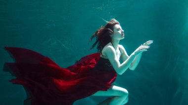 kırmızı elbiseli güzel kız su altında yüzer