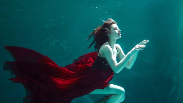 Kırmızı elbiseli güzel kız su altında yüzer — Stok fotoğraf