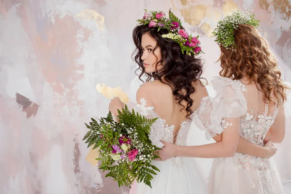 Two charming brides in beautiful spring wreaths on their heads. Beautiful young women in wedding dresses — Stock Photo, Image