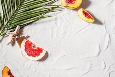 Plaj tatili Bir palmiye yaprağı, denizyıldızı ve beyaz ağaç dalı ve sulu meyveler beyaz kum üzerinde uzanır. Masaüstü duvar kağıdı.