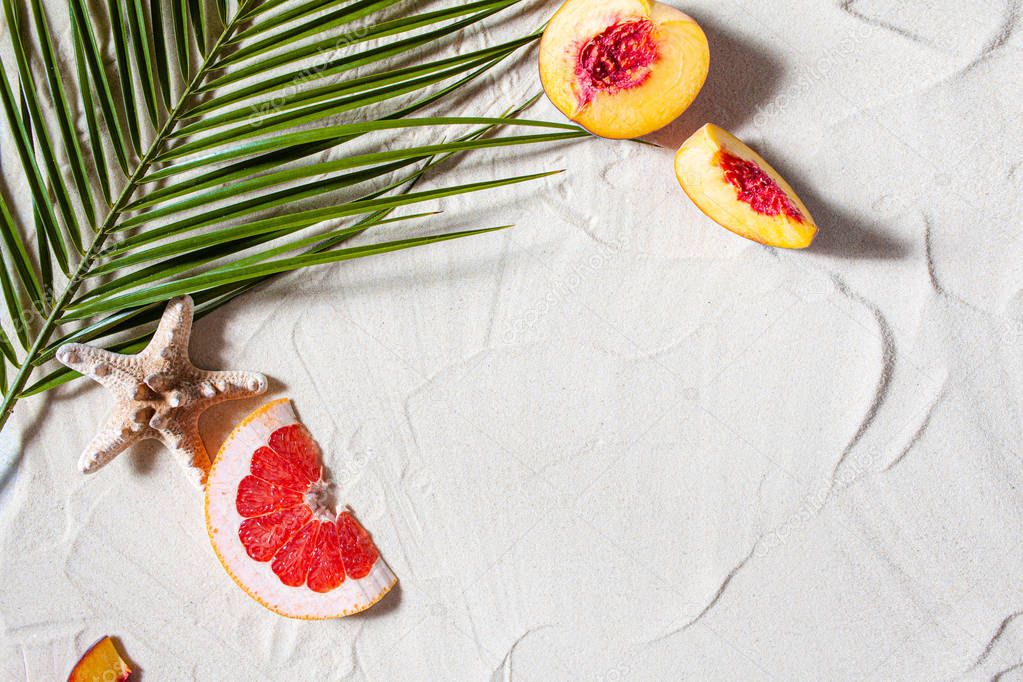 Beach vacation. A palm leaf and juicy fruits lie on white fine sand. Desktop wallpaper.