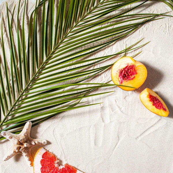 Plaj tatili Bir palmiye yaprağı, denizyıldızı ve beyaz ağaç dalı ve sulu meyveler beyaz kum üzerinde uzanır. Masaüstü duvar kağıdı.