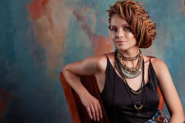 Südliches Aroma. stilvolle schöne junge Frau mit Afro-Zöpfen in hohe Haare gesteckt, sitzt im Stuhl in warmen Farben. — Stockfoto