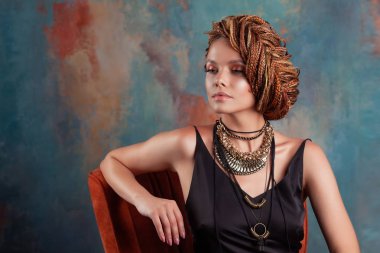 Güney lezzeti. Afro örgüleri ile şık güzel genç kadın yüksek saç içine sıkışmış, sıcak renklerde sandalyede oturan.