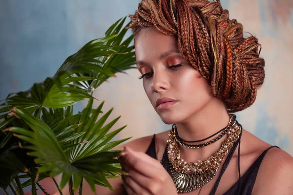 Южный вкус. Молодая загорелая женщина с афрокосичками улыбается, держа большой горшок с тропическим растением . — стоковое фото
