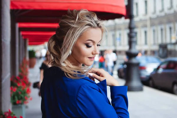 Při hledání kávy. Portrét krásné mladé ženy, blondýny na pozadí červených okýnků restaurací. — Stock fotografie
