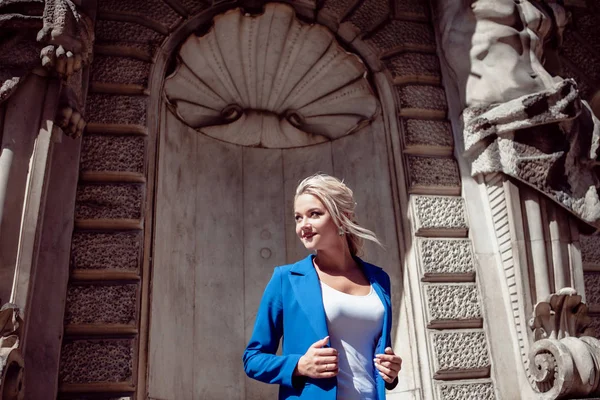 Promenera genom den historiska stadskärnan. Vacker flicka, blondin med en hästsvans i en blå pantsuit, mot historiska byggnader. — Stockfoto