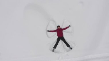 genç kadın karda bir kar meleği yapar, drone üst görünümü, rotasyon.