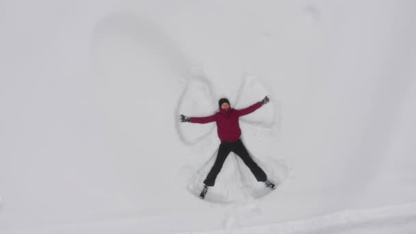 Giovane donna fa un angelo di neve nella neve, drone vista dall'alto, rotazione . — Video Stock