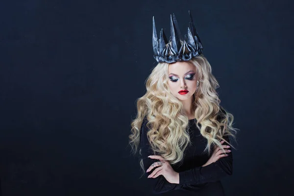 Retrato de uma rainha gótica. Mulher loira jovem bonita em coroa de metal e capa preta . — Fotografia de Stock