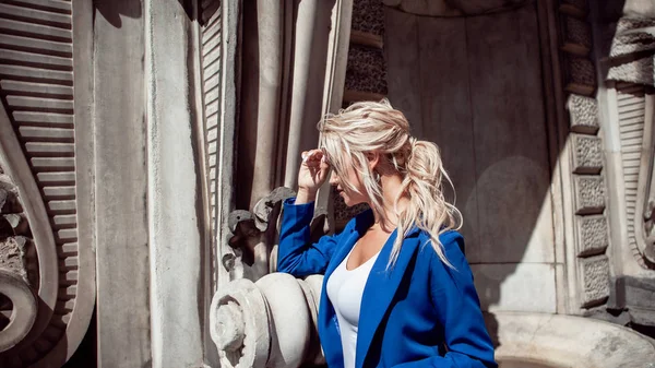 Caminhe pelo centro histórico. Menina bonita, loira com um rabo de cavalo em um terno azul, contra edifícios históricos . — Fotografia de Stock