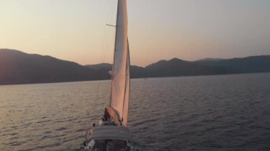 Yat, güzel beyaz bir yat kıyıdan ayrılıyor. Pembe gün batımı