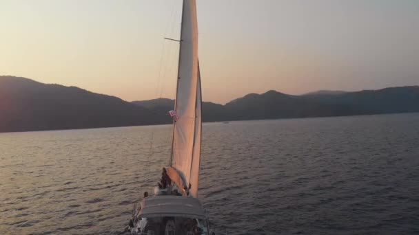 Яхтинг, красивая белая яхта отплывает от берега. Розовый закат — стоковое видео