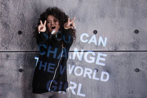 Curly Girl dansar mot bakgrund av grå vägg på vilken en mångfärgad motiverande inskription projiceras. — Stockfoto