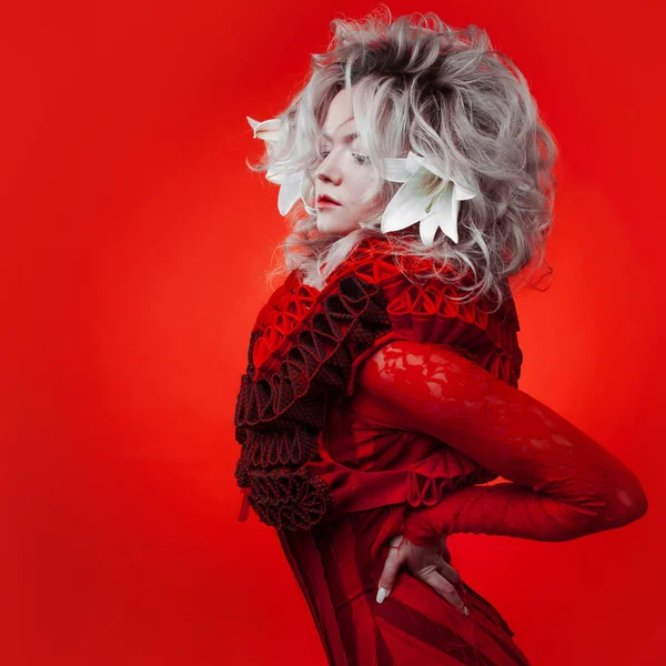 Tonos de rojo. Mujer atractiva, en un vestido rojo, posando sobre un fondo rojo, con flores de lirio blanco en el pelo . —  Fotos de Stock