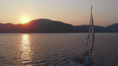 Yat, güzel beyaz bir yat kıyıdan ayrılıyor. Pembe gün batımı