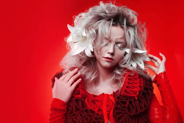 Tonos de rojo. Extraña mujer atractiva en un traje rojo, sobre un fondo rojo, con flores de lirio en el pelo . —  Fotos de Stock