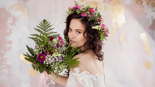 Elegante brunette meisje bruid met bloemen. Mooie jonge bruid in een weelderige bruiloft krans van verse bloemen — Stockfoto