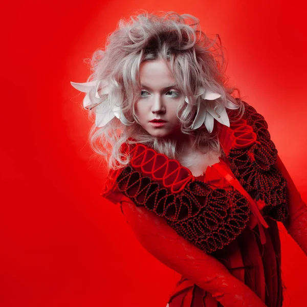 Shades of red. Strange attractive woman in a red outfit, on a red background, with lily flowers in her hair. — Stock Photo, Image