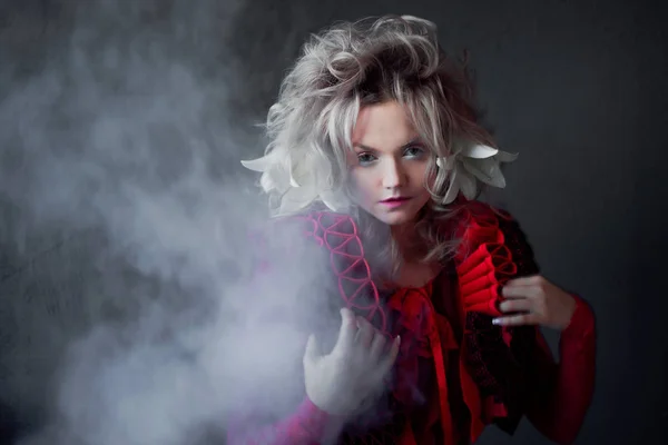 Tonos de rojo. Mujer atractiva, con maquillaje de moda, cuello en zigzag, posando en humo, con flores en el pelo . —  Fotos de Stock