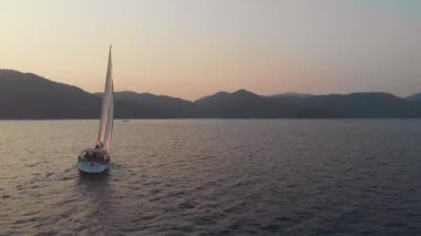 Yat, güzel beyaz bir yat kıyıdan ayrılıyor. Pembe gün batımı