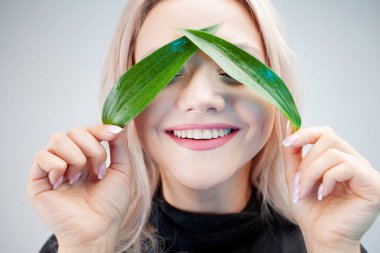 Doğal kozmetik, konsept. Çekici sarışın bitkinin yapraklarını gözlerine yapıyor.,