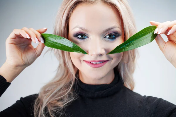 Cosméticos naturais, conceito. Adorável loira ri e aplica pétalas de plantas aos olhos como manchas nos olhos — Fotografia de Stock