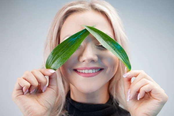 Natural cosmetics, concept. Adorable blonde laughs and applies plant petals to her eyes like eye patches — Stock Photo, Image