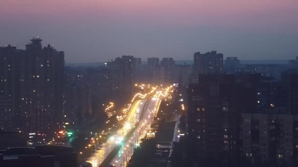 Avondstad in de waas, panorama van de stad met de snelweg, auto 's gaan met koplampen op. — Stockvideo