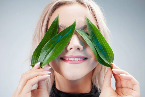 Natural cosmetics, concept. Adorable blonde laughs and applies plant petals to her eyes like eye patches — Stock Photo, Image