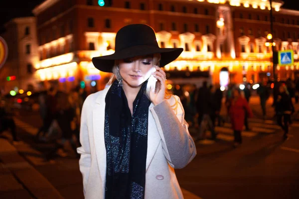 Snygg ung kvinna i en elegant beige rock talar i telefon, på en stadsgata på natten. — Stockfoto
