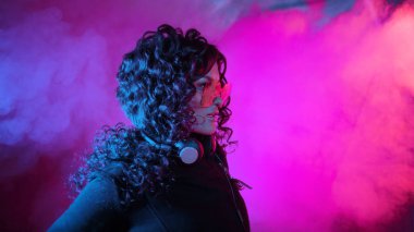 Büyük güneş gözlüklü genç, şık kıvırcık kadın, müziğe yöneliyor, kulaklıklarını çıkarıyor, dans ediyor, duvara yaslanıyor..