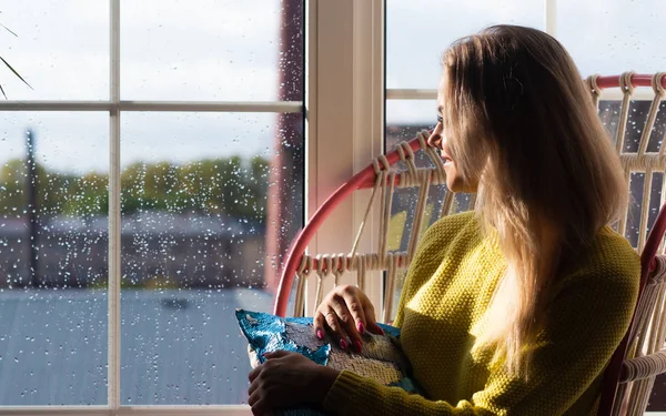 Chica tranquila en un suéter amarillo se sienta junto a la ventana y disfruta del día soleado . — Foto de Stock