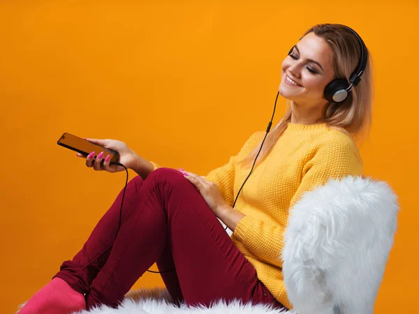 Happy and cheerful blonde music lover in headphones enjoys music and uses the music app in the smartphone