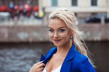 Güzel bir genç kadının yakın çekim portresi, uzun saçlı bir sarışın, saç modeli bukleler, at kuyruğu, elektrikli mavi ceketli.