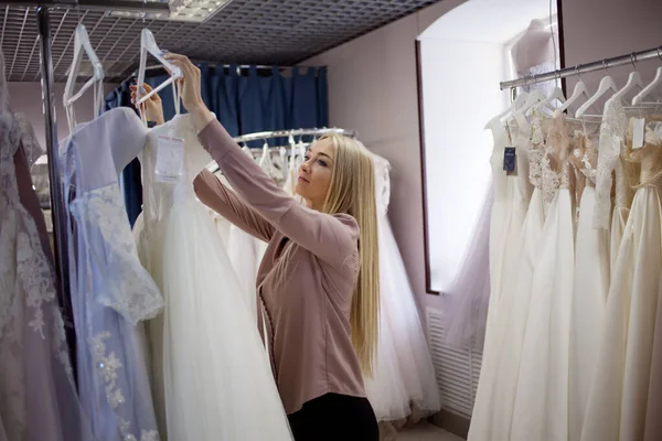 Junge blonde Frau wählt Hochzeitskleid in einem Hochzeitssalon. — Stockfoto