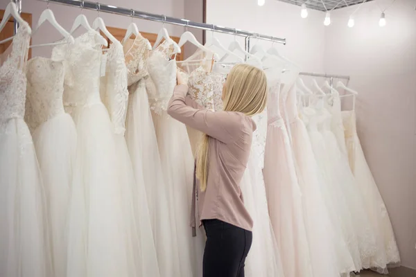 Fiatal szőke nő választ egy esküvői ruha egy esküvői szalonban. — Stock Fotó