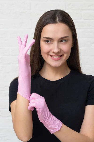 Mladá žena kosmetolog a obočí specialista nasadí ochranné rukavice a masku pro práci s klientem, — Stock fotografie