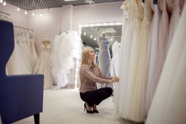 Genç sarışın kadın gelinliğini düğün salonundan seçiyor..