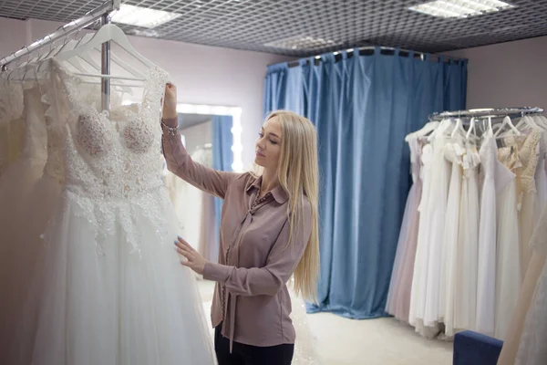Fiatal szőke nő választ egy esküvői ruha egy esküvői szalonban. — Stock Fotó