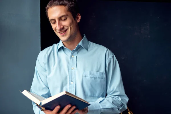 Jovem lendo um livro, um cara de camisa azul em um fundo azul escuro. — Fotografia de Stock