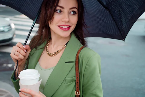 Jeune femme brune dans une veste verte sur une promenade. Belle fille avec café à emporter — Photo