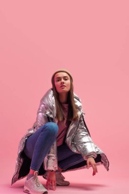 Parlak gümüş rengi ceketli ve örülmüş şapkalı havalı bir kız.,