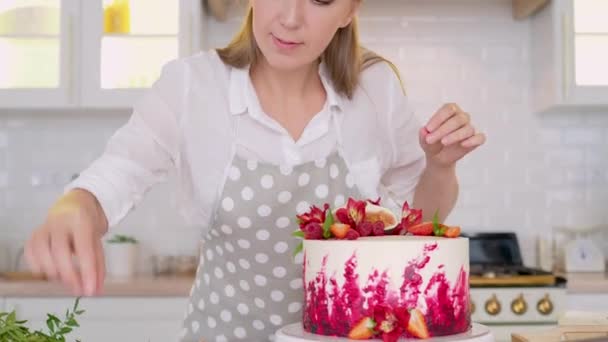 Kochen und Dekorieren von Kuchen mit Sahne. Junge Konditorin in der Küche dekoriert roten Samtkuchen — Stockvideo