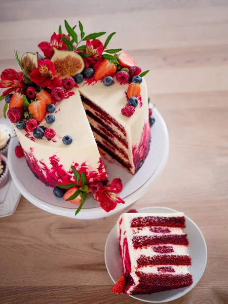 Grande bolo de veludo vermelho bonito, com flores e bagas em cima. Fatia em um prato, sobremesa. — Fotografia de Stock