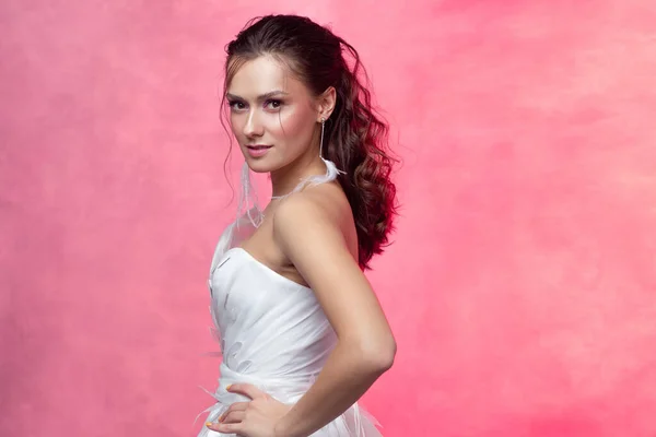 Porträtt av en ung vacker kvinna i elegant vit, strukturerad rosa bakgrund. — Stockfoto